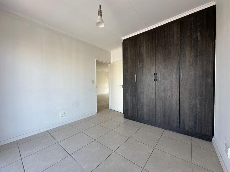 A clean, empty bedroom featuring neutral tiled flooring and dark wood-finish built-in cupboards, offering a versatile space ready for personalization.