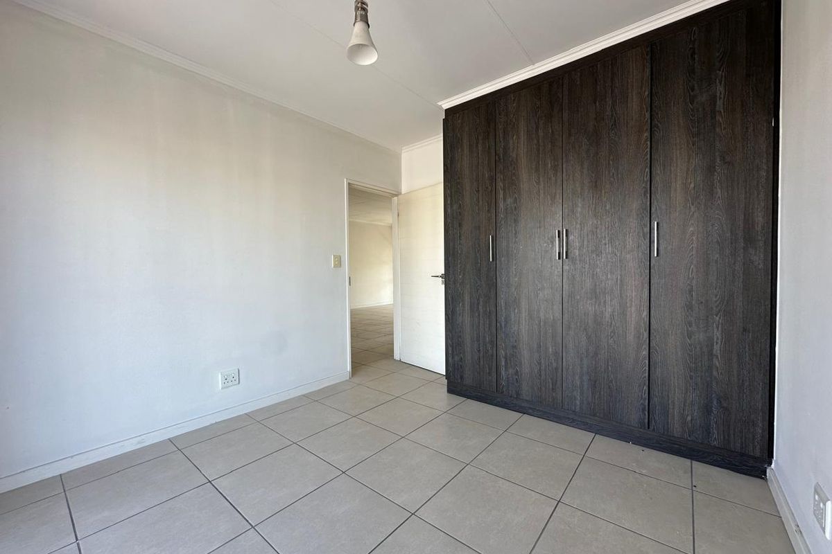 A clean, empty bedroom featuring neutral tiled flooring and dark wood-finish built-in cupboards, offering a versatile space ready for personalization.