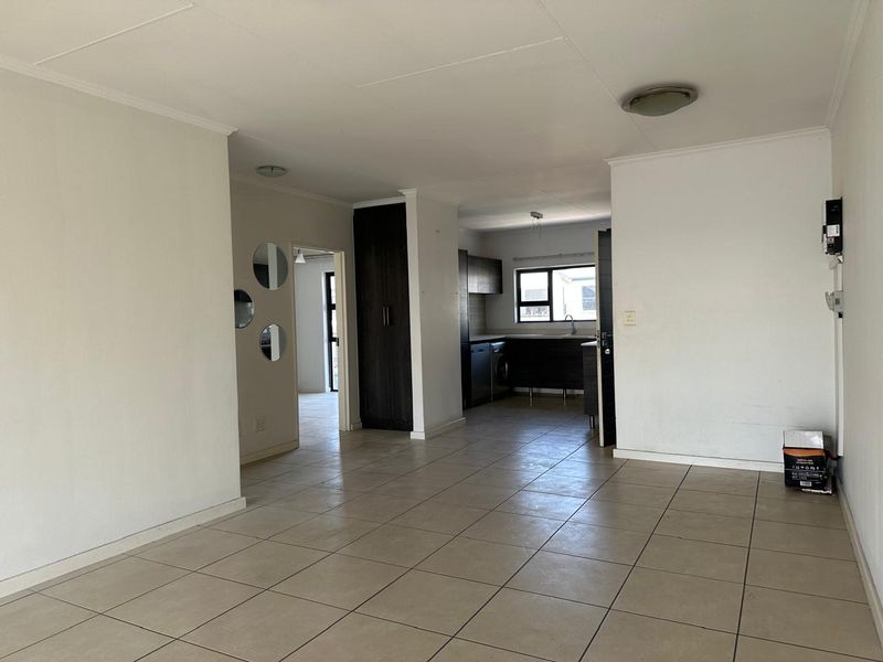 An open-plan living and kitchen area featuring neutral tiled flooring, dark built-in cabinetry, and a functional layout with direct access to adjacent rooms.