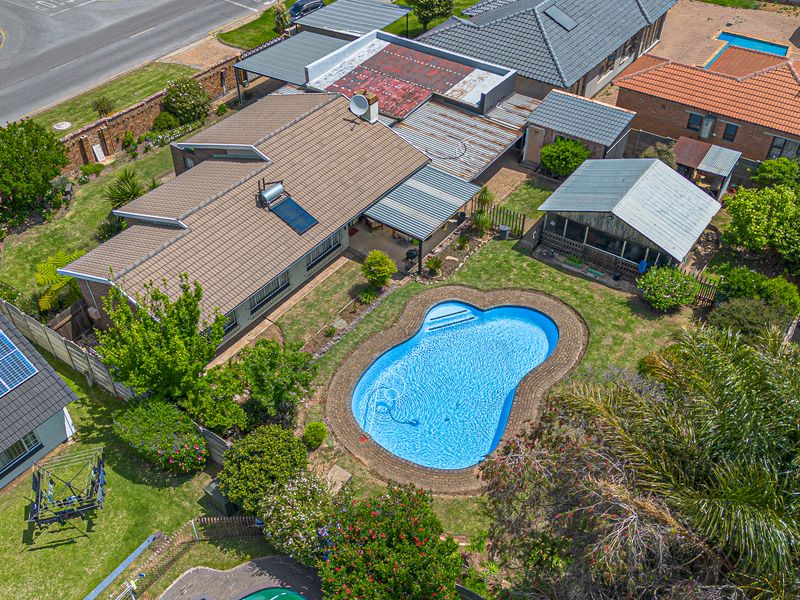 Aerial view of a residential property featuring a swimming pool, landscaped garden, and multiple roof structures including a solar water heater installation.