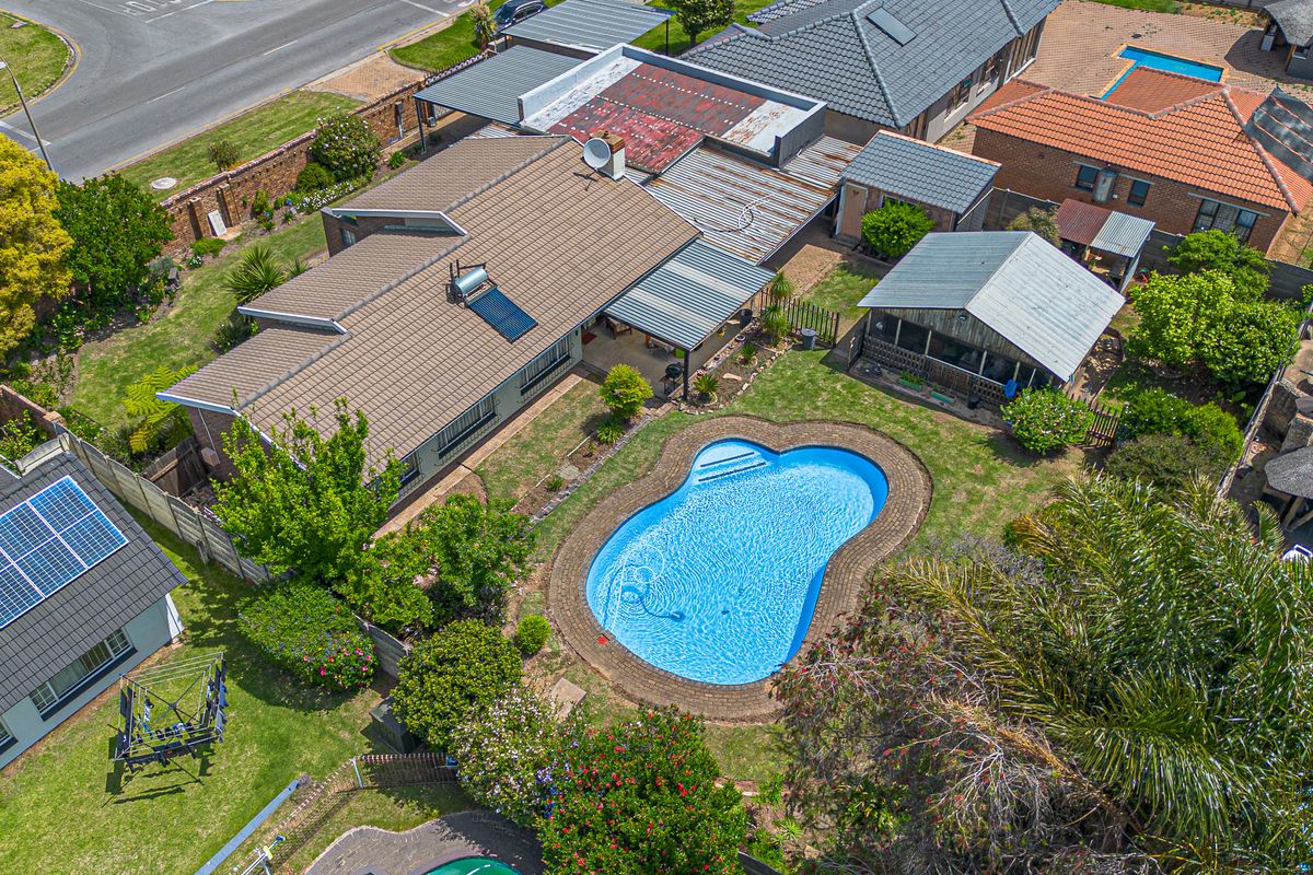 Aerial view of a residential property featuring a swimming pool, landscaped garden, and multiple roof structures including a solar water heater installation.