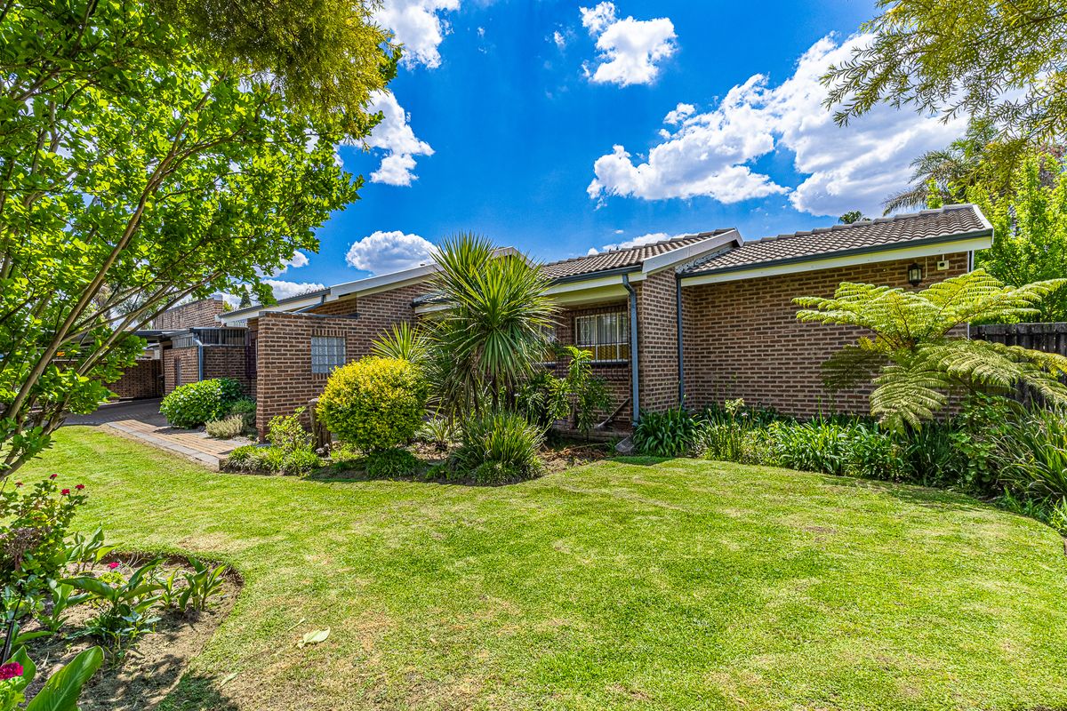 A well-maintained rear exterior view of the house featuring a classic brick facade, tiled roof, and a lush, landscaped garden with a paved walkway.