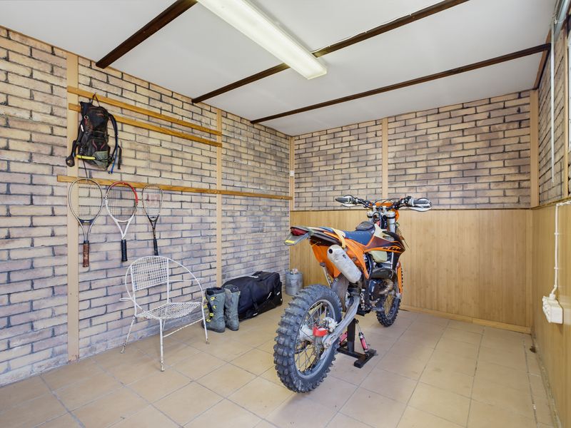 A functional garage space featuring exposed brick walls, tiled flooring, and timber paneling, suitable for vehicle storage or as a workshop area.