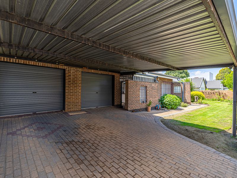 A spacious double garage with roller doors and an expansive covered carport area, featuring brick construction and a paved driveway.