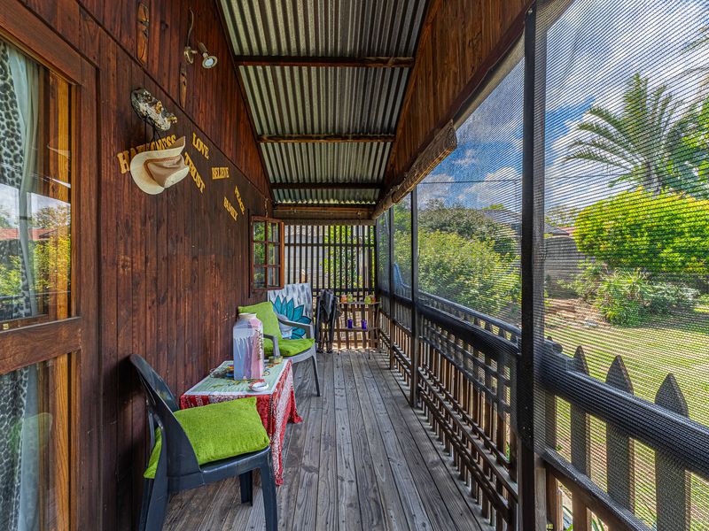 A rustic covered timber patio featuring corrugated metal roofing and mesh screening, overlooking a private garden area.