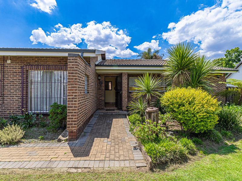 Front elevation of a brick house featuring a paved walkway leading to the entrance, complemented by established garden landscaping and security features.
