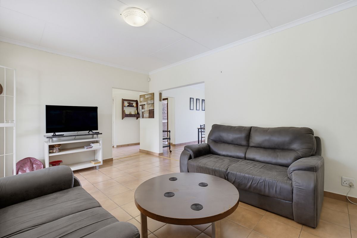 A functional living room featuring neutral tiled flooring and clean wall finishes, providing a versatile space with easy access to adjacent areas.