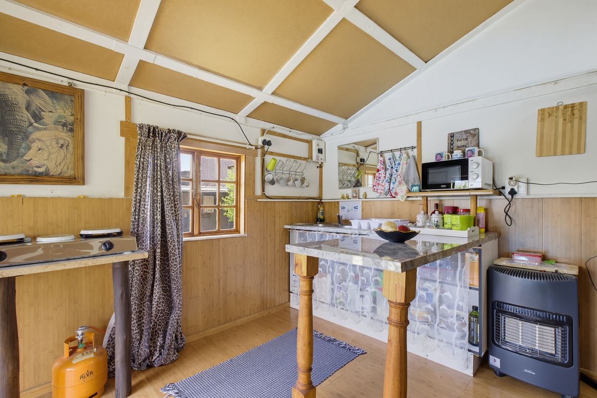 Compact kitchen area featuring timber wall paneling, stone countertop, and exposed beam ceiling, offering a rustic aesthetic with potential for modernization.