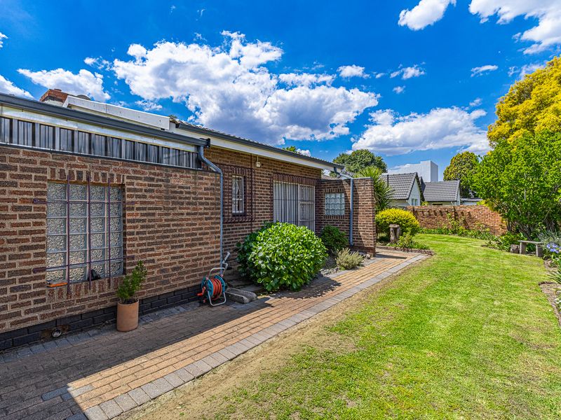 Rear view of the property featuring a face brick facade, glass block windows, security bars, and a paved walkway leading through the garden.