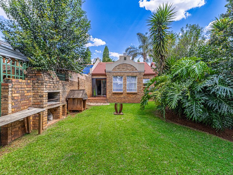 A well-maintained rear garden featuring a brick braai area, established landscaping, and a clear view of the property's rear brick facade.