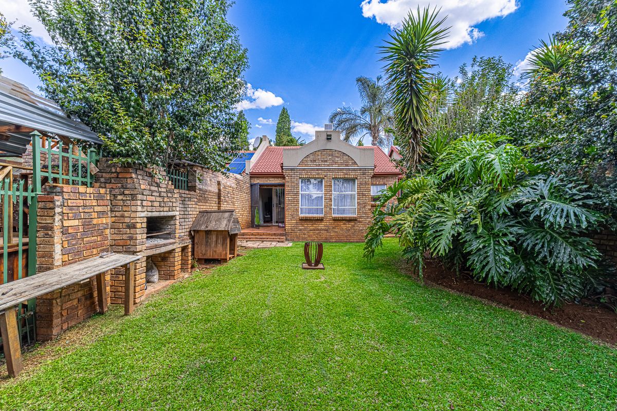 A well-maintained rear garden featuring a brick braai area, established landscaping, and a clear view of the property's rear brick facade.