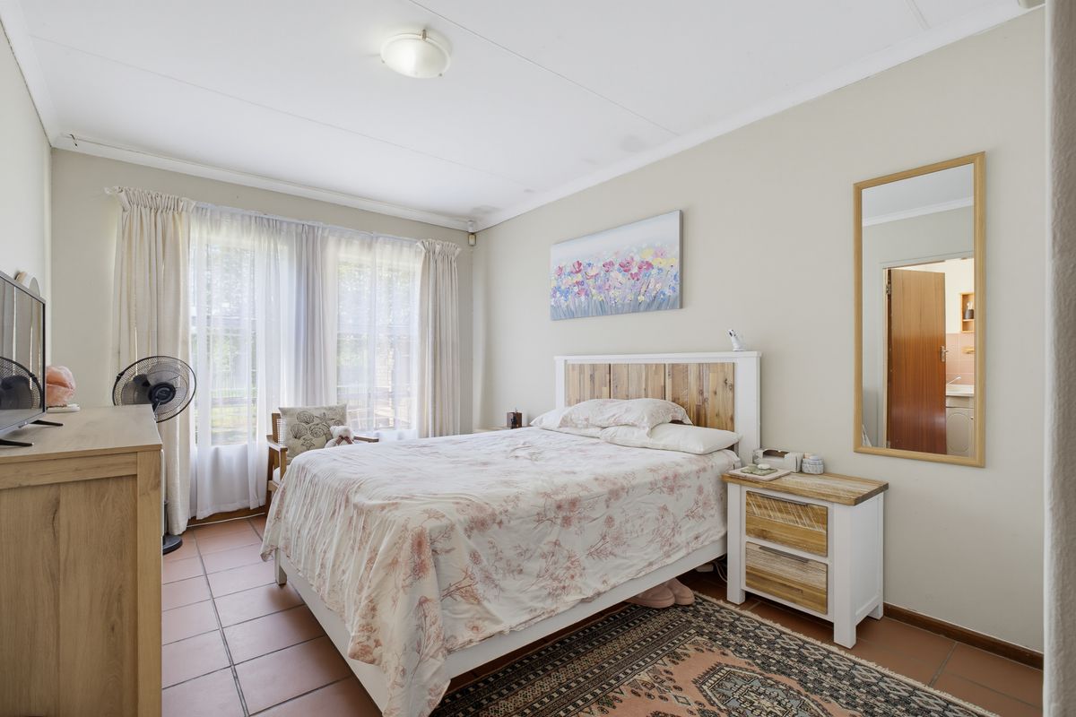 A well-lit bedroom featuring tiled flooring and large windows with curtain tracks, offering a functional and comfortable living space.