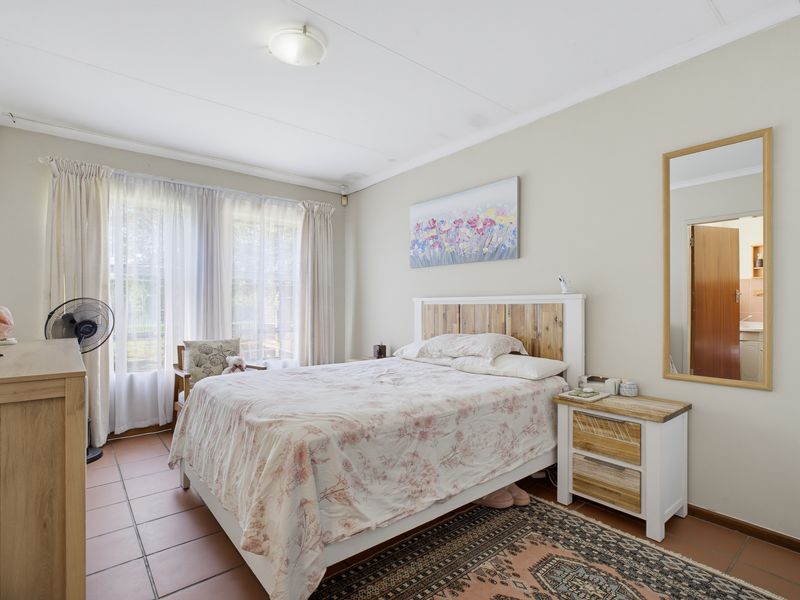 A well-lit bedroom featuring tiled flooring and large windows with curtain tracks, offering a functional and comfortable living space.