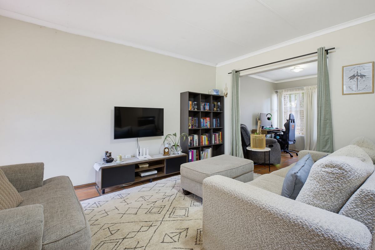 A comfortable living room featuring neutral walls, tiled flooring, and an open transition to an adjacent office space.