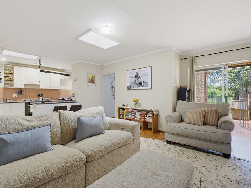 Open plan living area featuring terracotta flooring, skylights, and a functional kitchen with built-in cabinetry, flowing out to a private patio area.