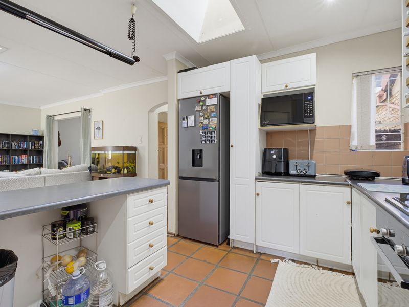 Open plan kitchen featuring white cabinetry, tiled flooring, a skylight, and integrated appliances, flowing into the adjacent living area.