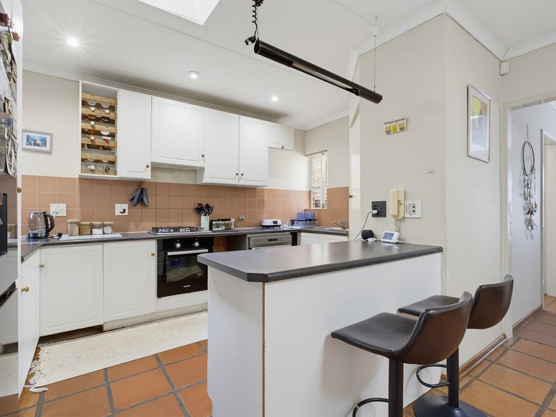 Functional kitchen featuring white cabinetry, dark laminate countertops, a breakfast bar, and terracotta floor tiles, providing a practical layout for daily use.