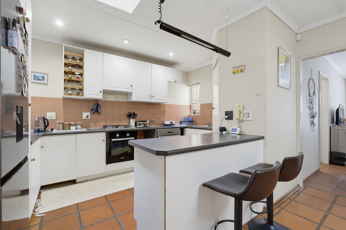 Functional kitchen featuring white cabinetry, dark laminate countertops, a breakfast bar, and terracotta floor tiles, providing a practical layout for daily use.