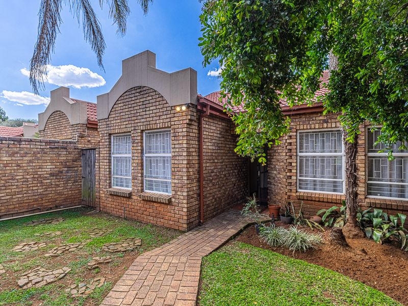 A rear view of the apartment featuring a face brick facade, tiled roof, paved walkway, and a small private garden area.