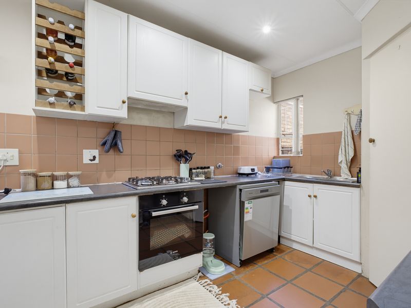 A functional kitchen featuring white cabinetry, a gas hob, built-in oven, tiled backsplash, and terracotta floor tiles.