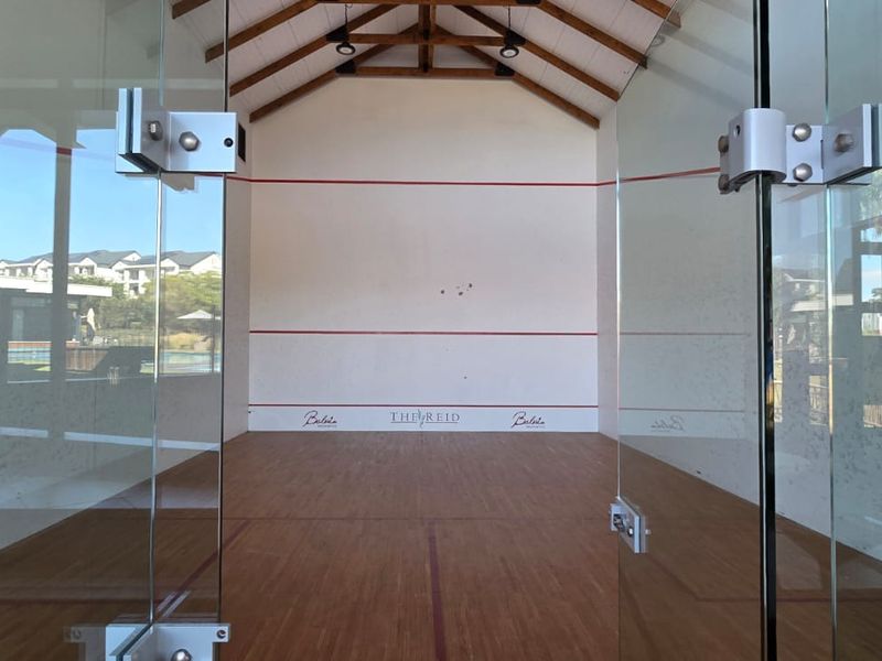 A well-maintained indoor squash court featuring timber flooring, glass walls, and exposed roof trusses within a residential estate facility.