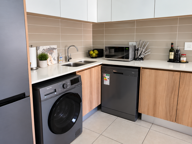 Modern kitchen featuring sleek two-tone cabinetry, quartz countertops, tiled backsplash, and integrated appliances including a dishwasher and washing machine.