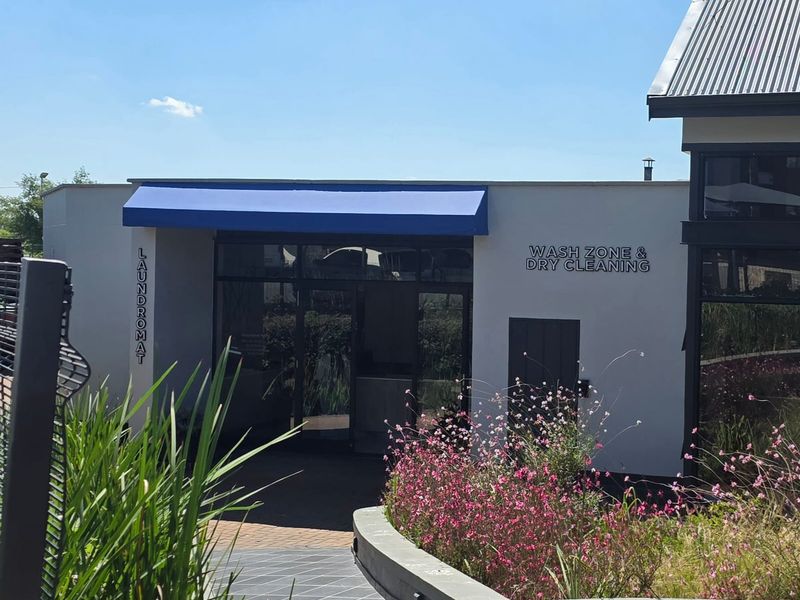 Exterior view of a commercial laundry and dry cleaning facility with a blue awning and glass entrance.