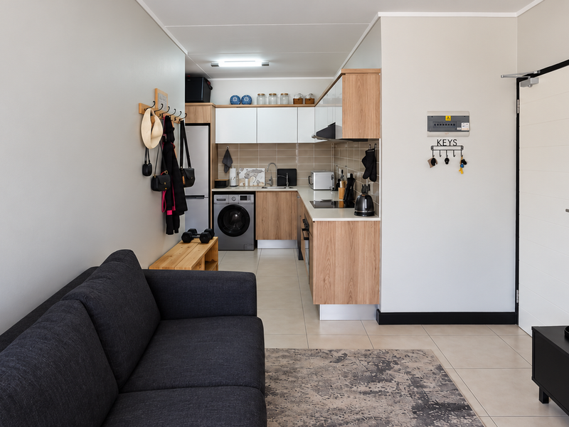 A modern open-plan living area featuring a compact, well-equipped kitchen with wood-finish cabinetry, tiled backsplash, and integrated appliances, seamlessly flowing into the living space.