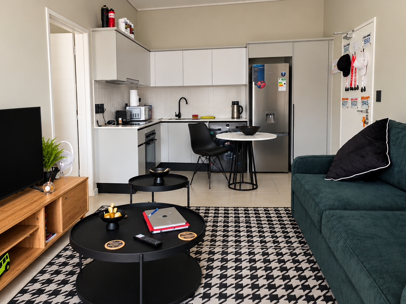 Modern open-plan living area featuring a compact, well-appointed kitchen with built-in cabinetry, integrated appliances, and neutral tiled flooring throughout.
