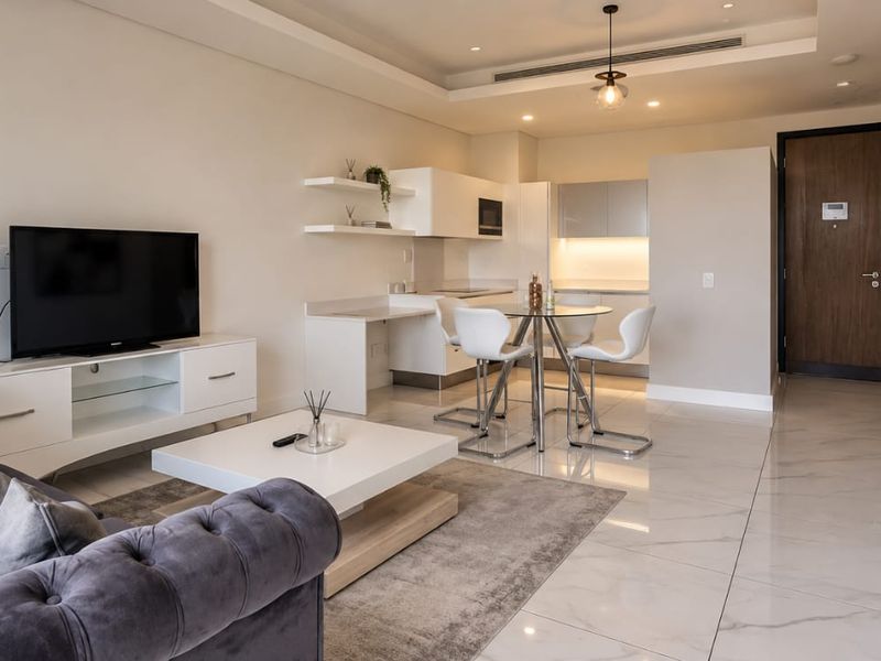 Modern open-plan living and kitchen area featuring high-quality marble-look floor tiles, recessed ceiling lighting, and sleek built-in cabinetry with integrated appliances.