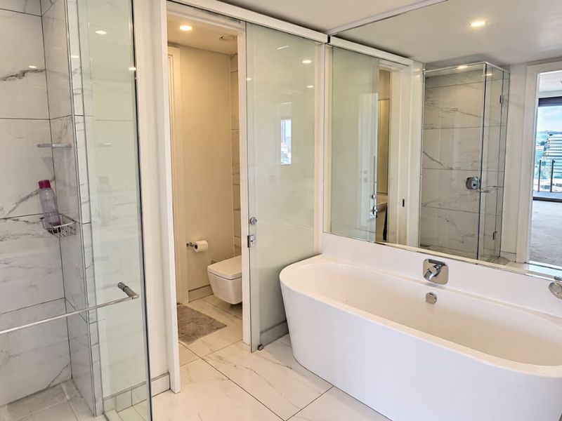 Modern bathroom featuring a freestanding bathtub, glass-enclosed shower, wall-mounted toilet, and elegant marble-look tiling with a large vanity mirror.