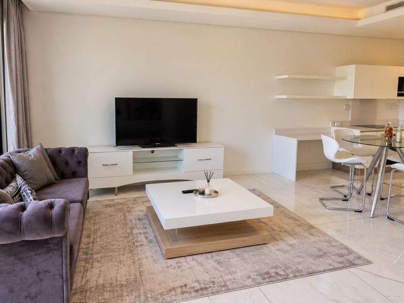 Modern open-plan living and kitchen area featuring sleek cabinetry, integrated appliances, tiled flooring, and large sliding doors leading to a balcony with city views.