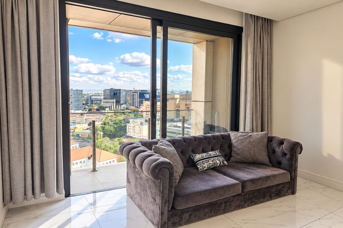 Modern living area featuring large sliding glass doors that open onto a balcony with expansive city views and high-quality tiled flooring.