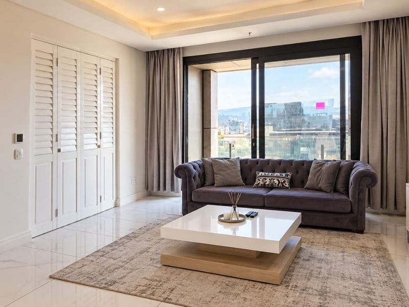 A bright and modern living room featuring polished tiled floors, recessed ceiling lighting, and large sliding glass doors leading to an outdoor balcony area.