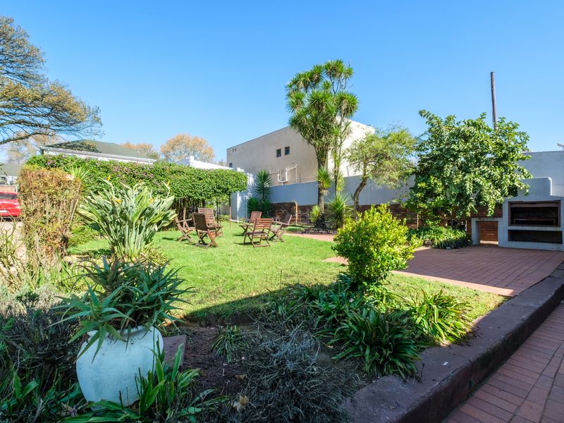 A private rear garden featuring a lawn, established landscaping, a paved patio area, and a built-in braai facility.
