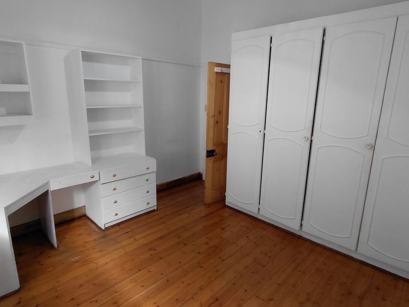 A bedroom featuring polished timber flooring, built-in cabinetry including a desk and shelving unit, and a large four-door built-in wardrobe.