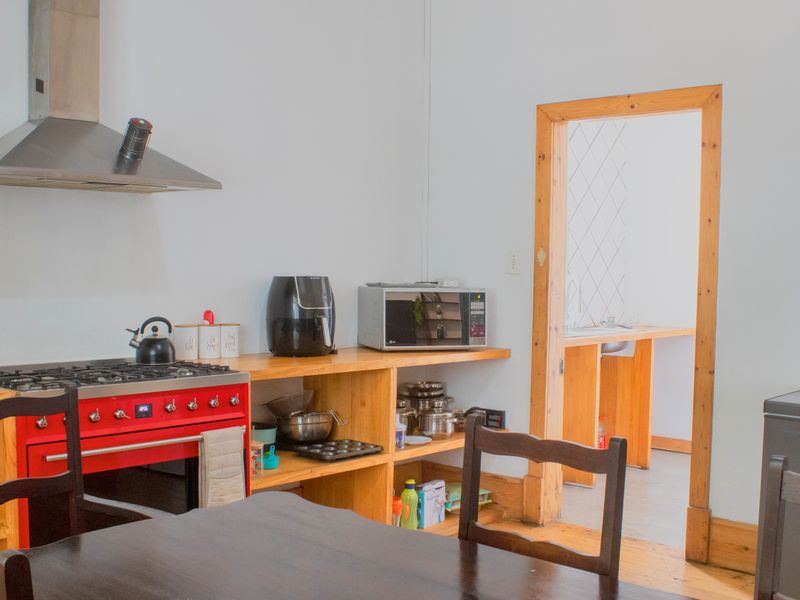 Kitchen area featuring a red gas stove, stainless steel extractor fan, and open wooden shelving, with an adjacent scullery visible through the doorway.