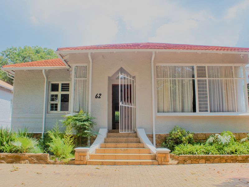 Front elevation of a single-story house featuring a tiled roof, stone-clad base, paved driveway, and a central entrance with a security gate.