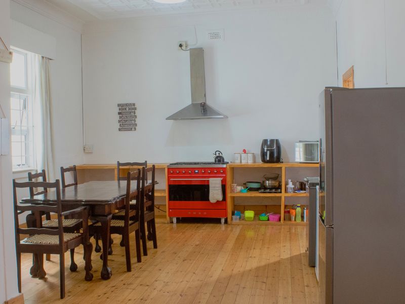 A kitchen featuring timber flooring, a pressed metal ceiling, open shelving, and a prominent red freestanding oven with an extractor fan.