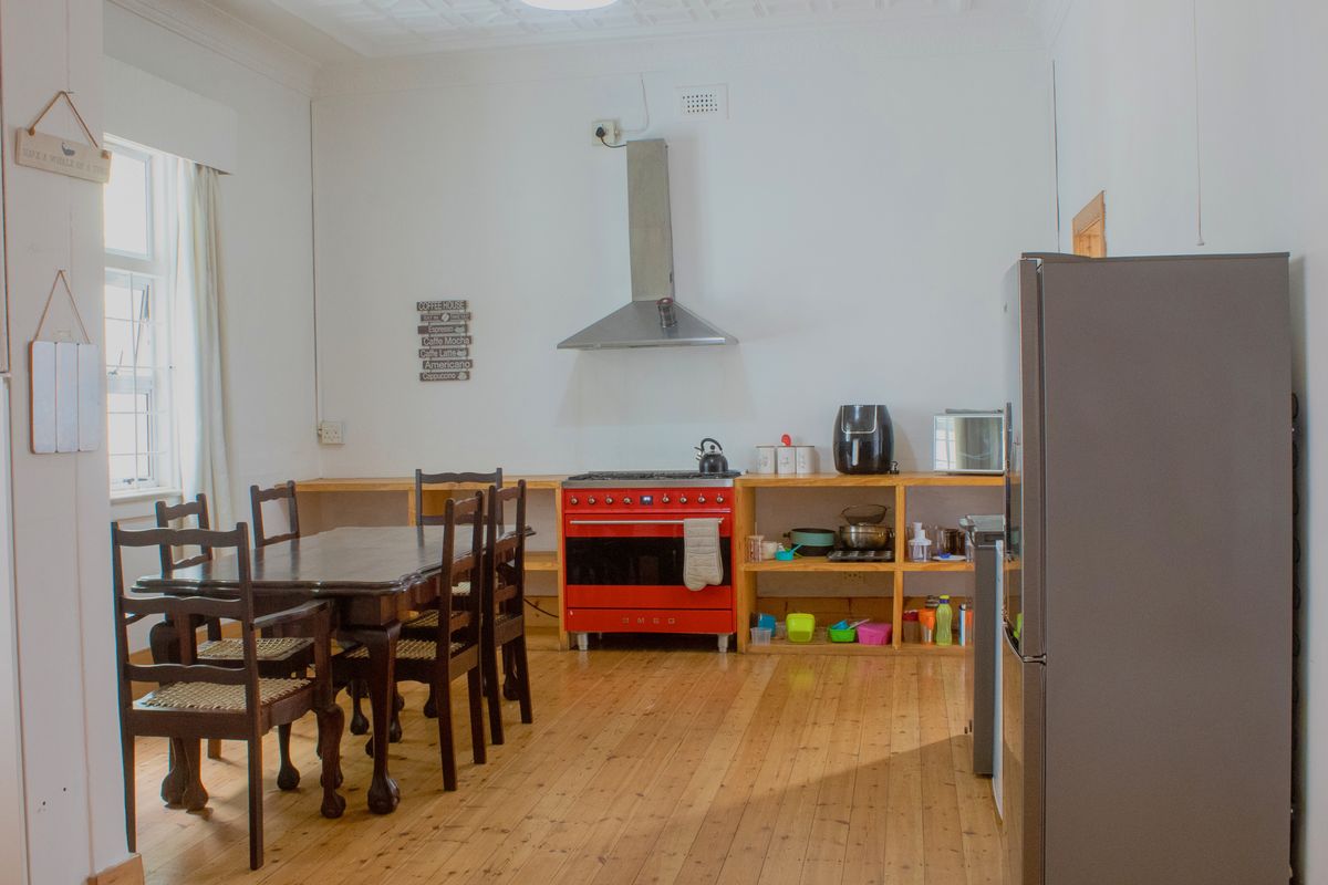 A kitchen featuring timber flooring, a pressed metal ceiling, open shelving, and a prominent red freestanding oven with an extractor fan.