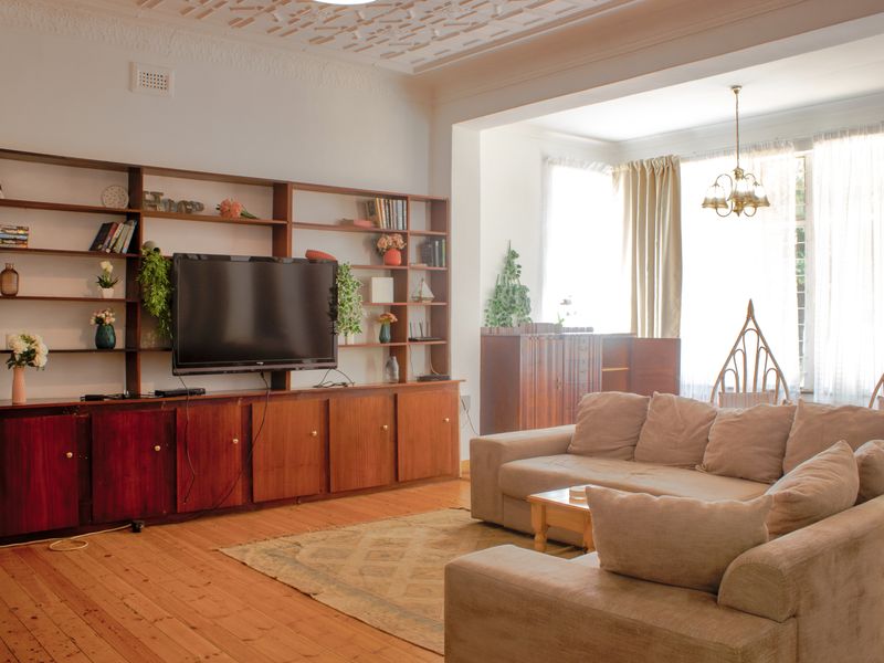Spacious living room featuring original hardwood flooring, ornate ceiling plasterwork, and a large built-in wooden shelving unit with integrated cabinetry.