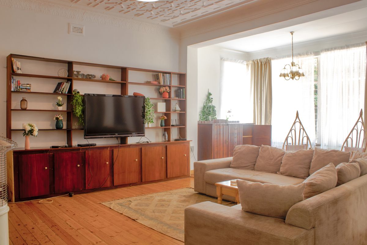 Spacious living room featuring original hardwood flooring, ornate ceiling plasterwork, and a large built-in wooden shelving unit with integrated cabinetry.