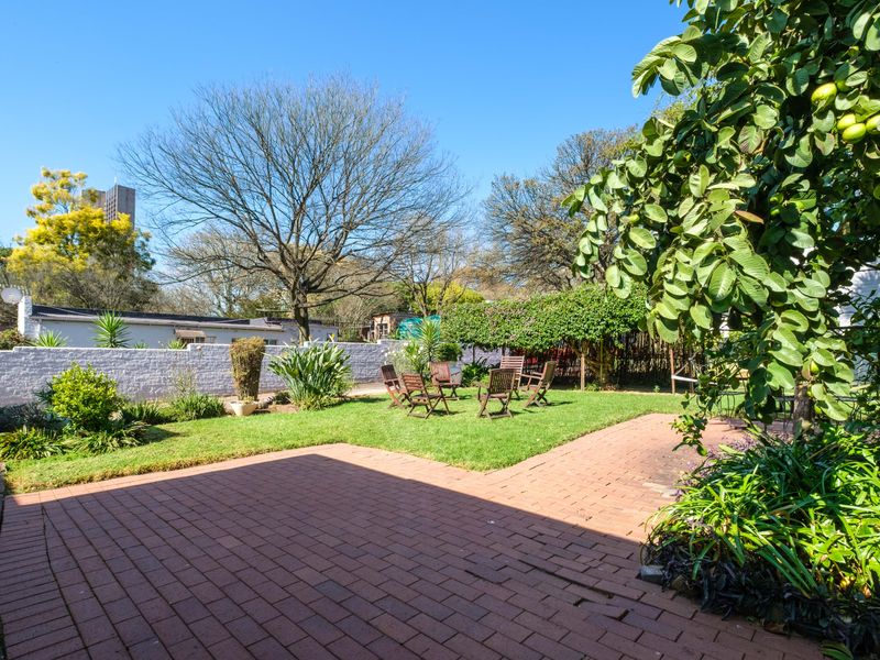 A spacious rear garden featuring a brick-paved patio area, a well-maintained lawn, and established perimeter walls with mature trees.