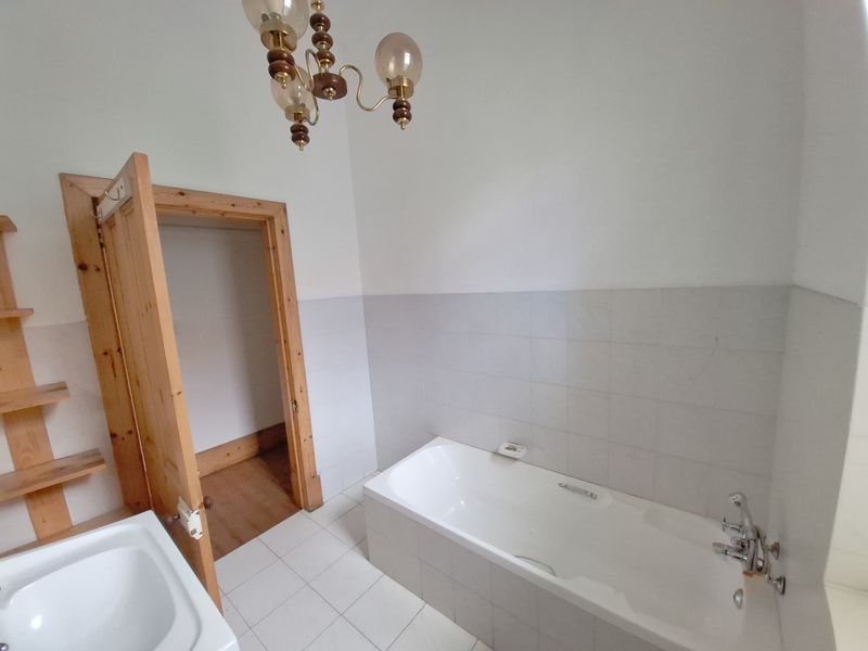 A functional bathroom featuring a built-in bathtub, tiled splashback, and tiled flooring, offering a clean and simple layout ready for modernization.