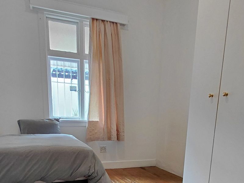A simple bedroom featuring timber flooring, a built-in wardrobe, and a window fitted with security bars.