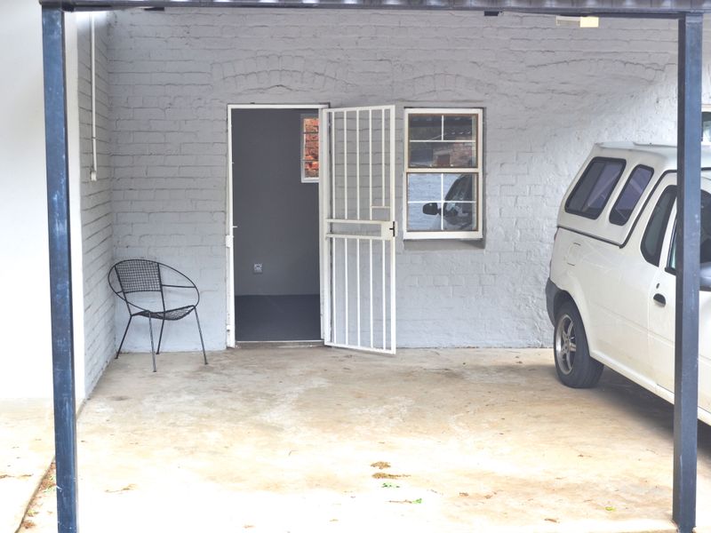A covered carport area featuring painted brick walls, a security gate, and a window, providing functional outdoor vehicle storage space.