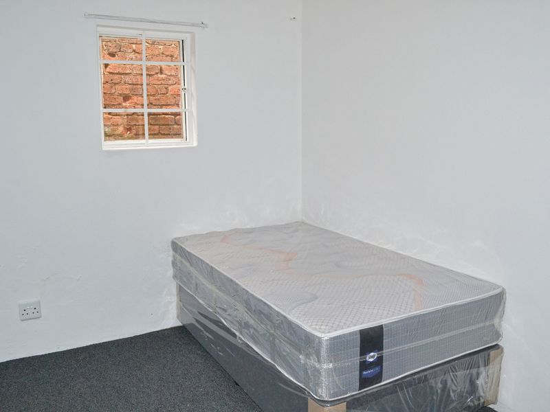 A simple bedroom featuring white walls, carpet flooring, and a small window, providing a blank canvas for potential interior design and furnishing.