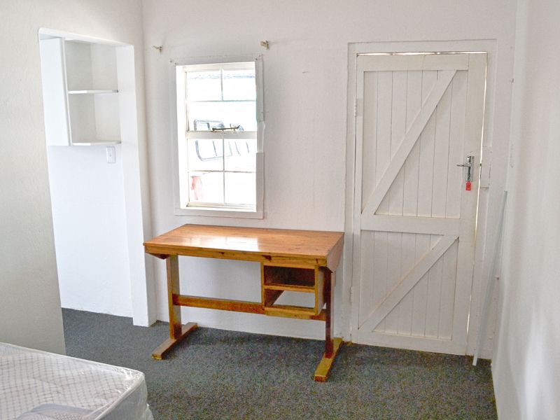 A simple bedroom featuring a sash window, built-in shelving, and a traditional braced timber door, requiring cosmetic updates to improve its overall appeal.