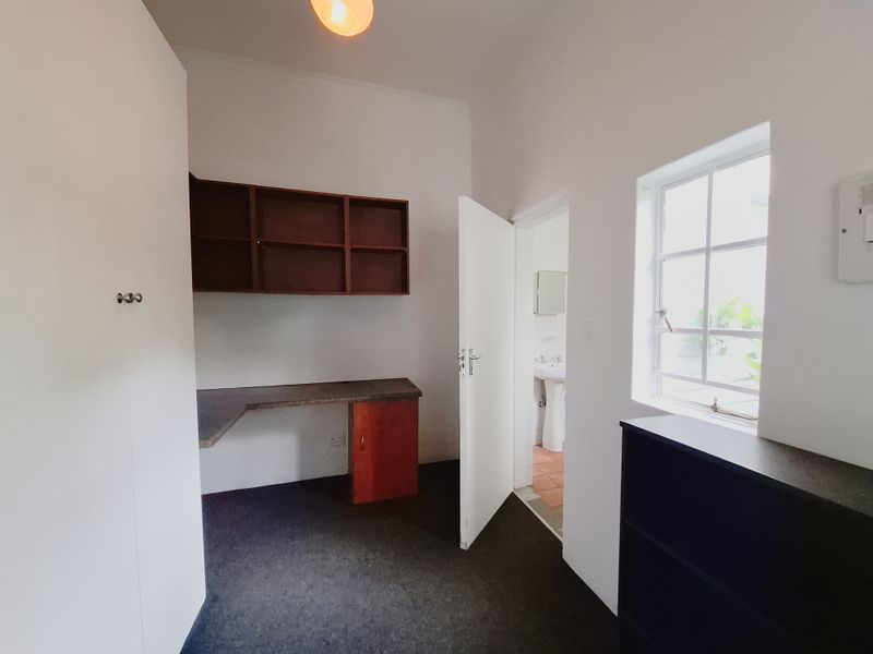 A functional home office space featuring a built-in desk, wall-mounted shelving, and a multi-pane window, with direct access to an adjacent bathroom.