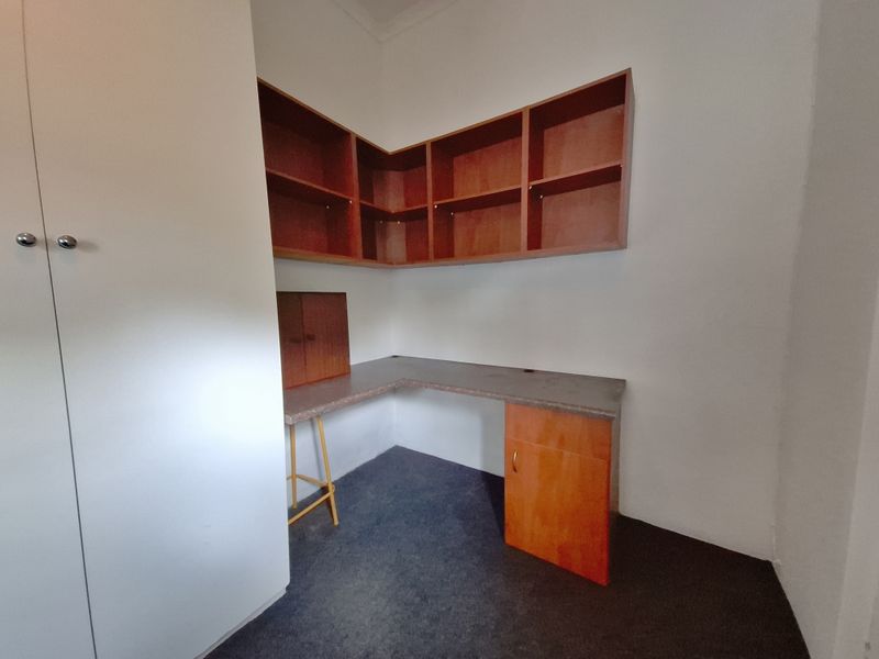 A functional home office space featuring built-in wooden desk, overhead shelving, and a large built-in storage cupboard.